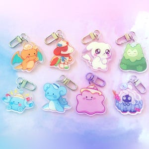 May include: Collection of eight colorful acrylic keychains featuring various cartoon characters. Each keychain has a silver clasp for easy attachment. The characters include a dragon, a dog-like figure, a white rabbit, and a green plant-like creature.