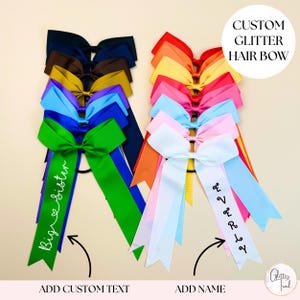 May include: A selection of vibrant glitter hair bows with long ribbons. The bows are in a range of colours, such as blue, green, pink, and yellow. Some ribbons feature custom text, and the image includes the text "CUSTOM GLITTER HAIR BOW".