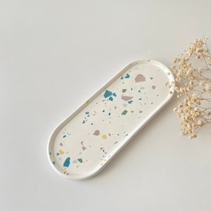 Op de afbeelding: Witte ovale dienblad met een terrazzo-patroon in tinten blauw, groen, roze en geel.