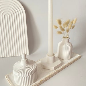 Könnte beinhalten: Weiße Keramik-Schale mit strukturierter Oberfläche, mit einem weißen Kerzenhalter, einer weißen Vase mit getrocknetem Pampasgras und einem weißen, gedeckten Krug mit geriffeltem Design.