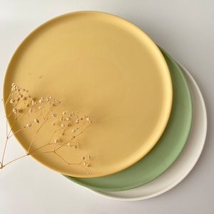 以下が含まれることがあります： 黄色、緑、白のセラミック製のプレートが3枚重ねられています。一番上のプレートは黄色、真ん中のプレートは緑、一番下のプレートは白です。