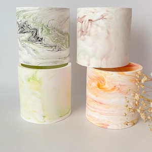 May include: Four cylindrical concrete planters with marbled patterns. The planters are in shades of green, pink, yellow, and orange.