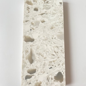 May include: A close-up of a white quartz countertop with a swirling pattern of gray and white veins. The surface has a speckled appearance with small, irregular holes.