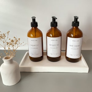 Könnte beinhalten: Drei bernsteinfarbene Glasflaschen mit schwarzen Pumpen und weißen Etiketten. Die Etiketten lauten "refresh & clean" und die Produktnamen: "Shampoo", "Duschgel" und "Haarbalsam".