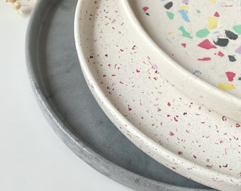 May include: Three round trays, one gray, one white with red speckles, and one white with multi-colored speckles. The trays are stacked on top of each other.