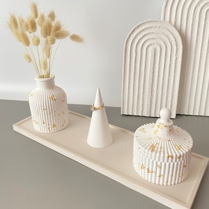 May include: White ceramic tray with a white ceramic vase with gold flecks, a white ceramic ring holder, and a white ceramic lidded box with gold flecks. The tray is on a gray surface.