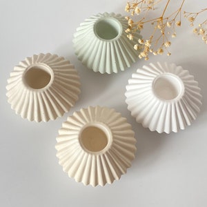 May include: Four ceramic candle holders in white and light green with a fluted design. The holders are arranged in a circle on a white surface.