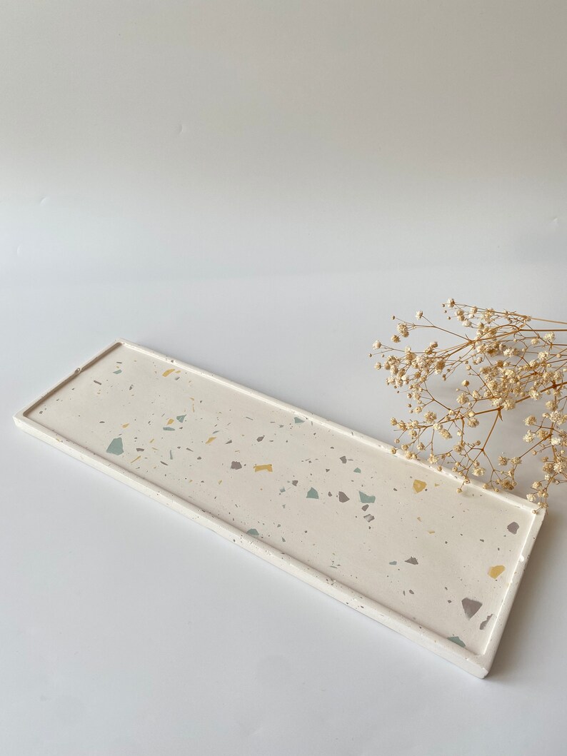Pode incluir: Uma bandeja retangular com base branca e um padr&atilde;o de terrazzo em tons de amarelo, verde e cinza. A bandeja tem uma borda ligeiramente elevada.