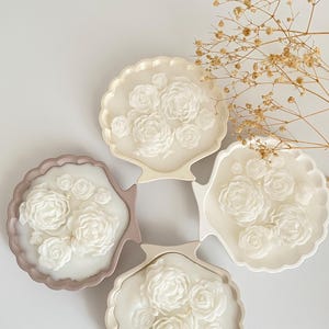May include: Four white floral candles in seashell-shaped holders. The holders are in shades of beige and light brown.