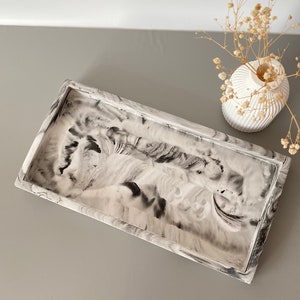 May include: A rectangular tray with a white and black marbled design. The tray has a raised edge and is made of a smooth, glossy material.
