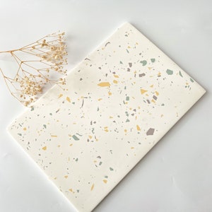 May include: A white rectangular serving tray with a terrazzo pattern featuring yellow, green, and brown flecks.