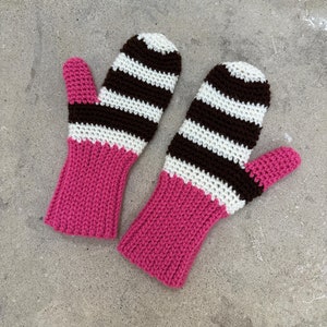 May include: A pair of crocheted mittens with brown and white stripes and pink cuffs.