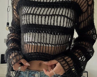 May include: A black crochet sweater with a striped pattern. The sweater is loose-fitting and has long sleeves.