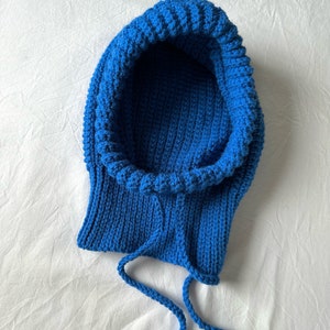 Puede incluir: Una bufanda de punto azul con capucha y cord&oacute;n.