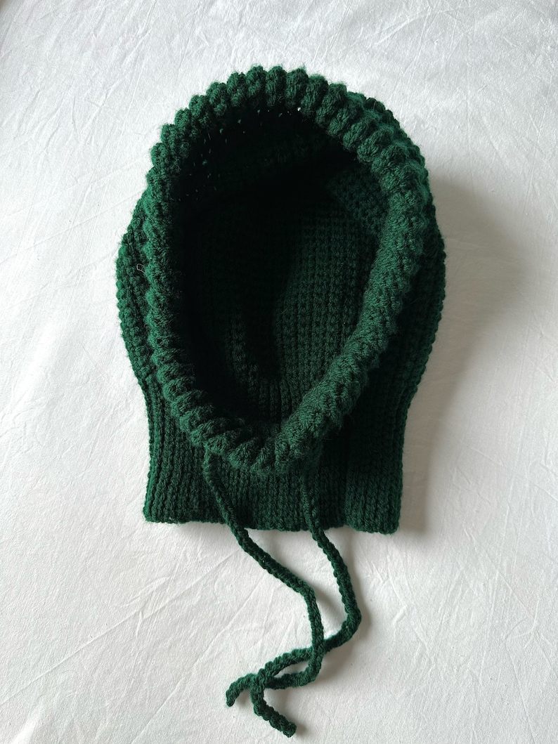 Puede incluir: Una bufanda de punto con capucha de color verde oscuro con cord&oacute;n.