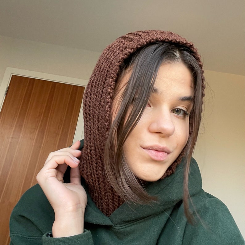 May include: A brown knitted hooded scarf with a long neck covering. The scarf is worn by a person with long brown hair.