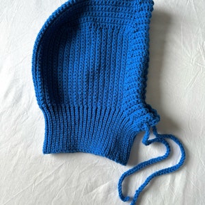 Puede incluir: Un gorro azul de punto de ganchillo con una larga corbata. El gorro est&aacute; hecho con un punto sencillo y tiene un ajuste holgado.