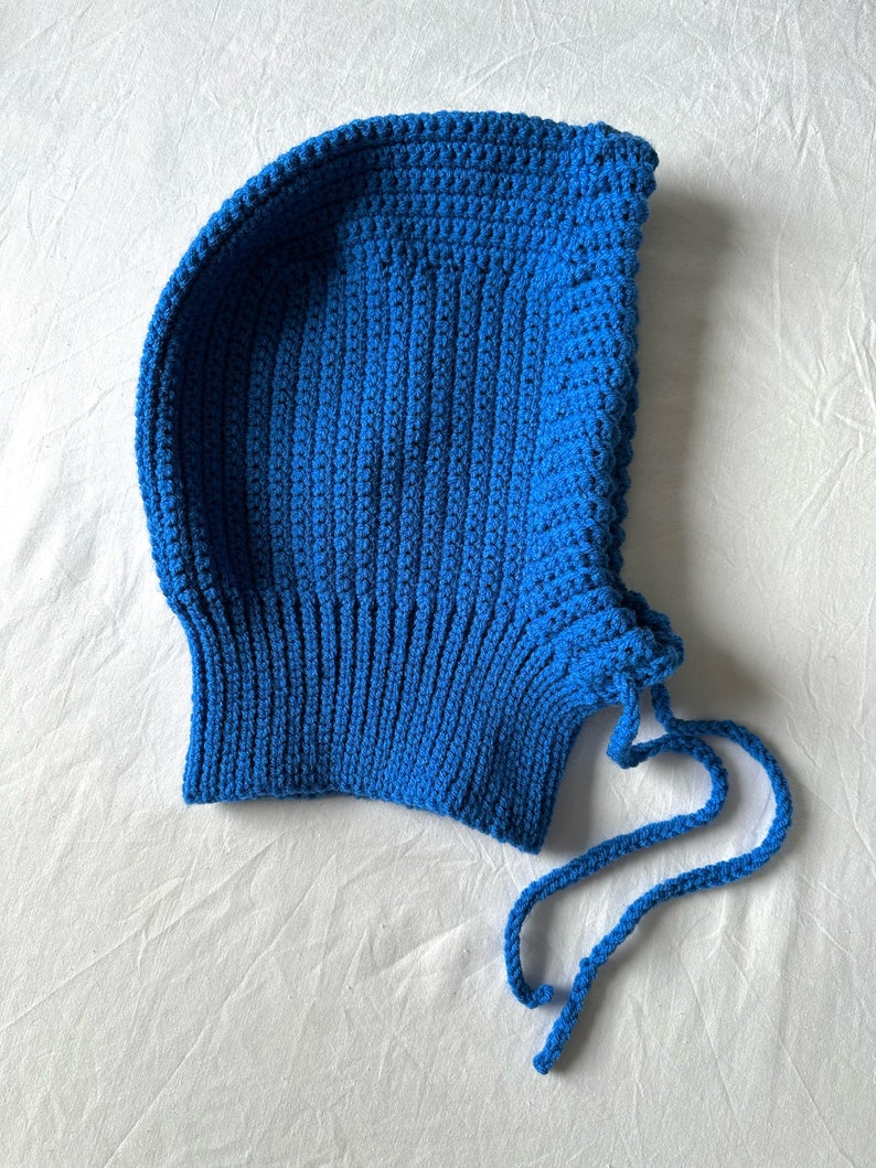 Puede incluir: Un gorro azul de punto de ganchillo con una larga corbata. El gorro est&aacute; hecho con un punto sencillo y tiene un ajuste holgado.