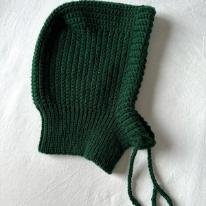 Puede incluir: Un gorro de punto verde oscuro con capucha y una larga cuerda de corbata.
