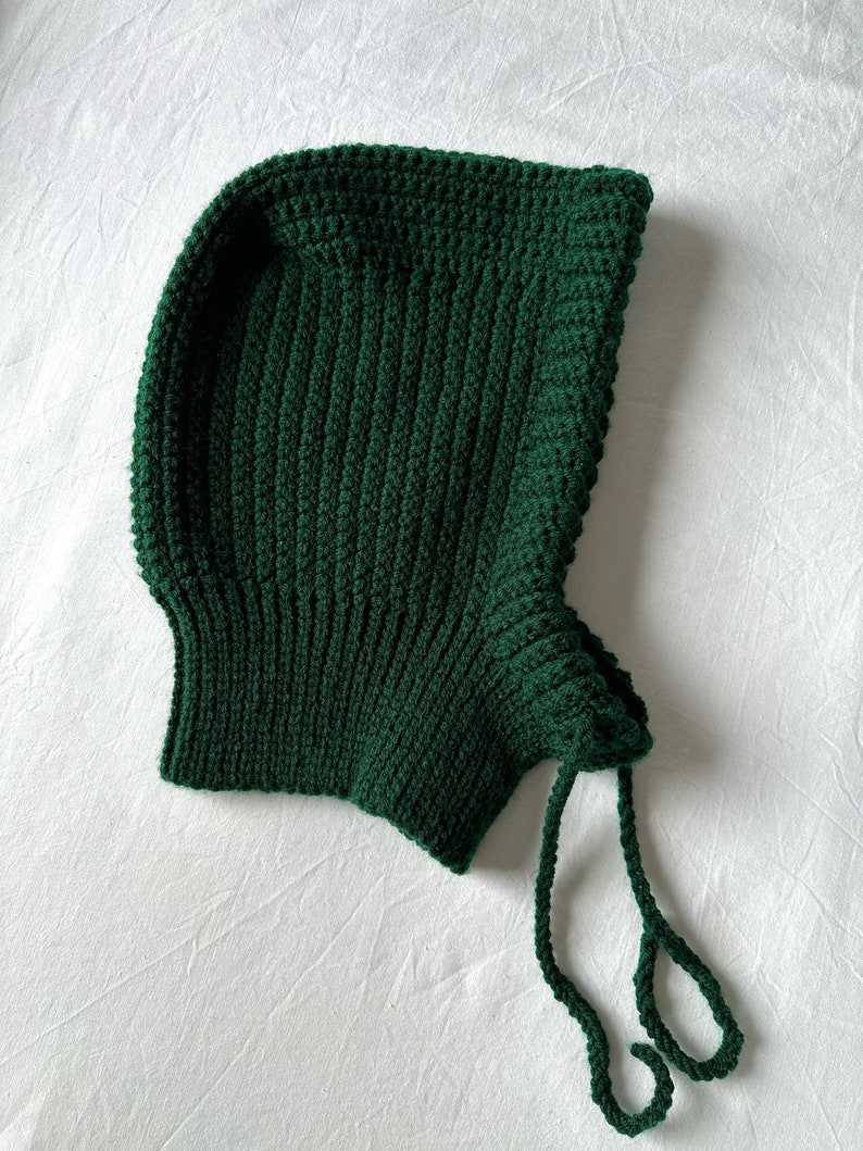 Puede incluir: Un gorro de punto verde oscuro con capucha y una larga cuerda de corbata.