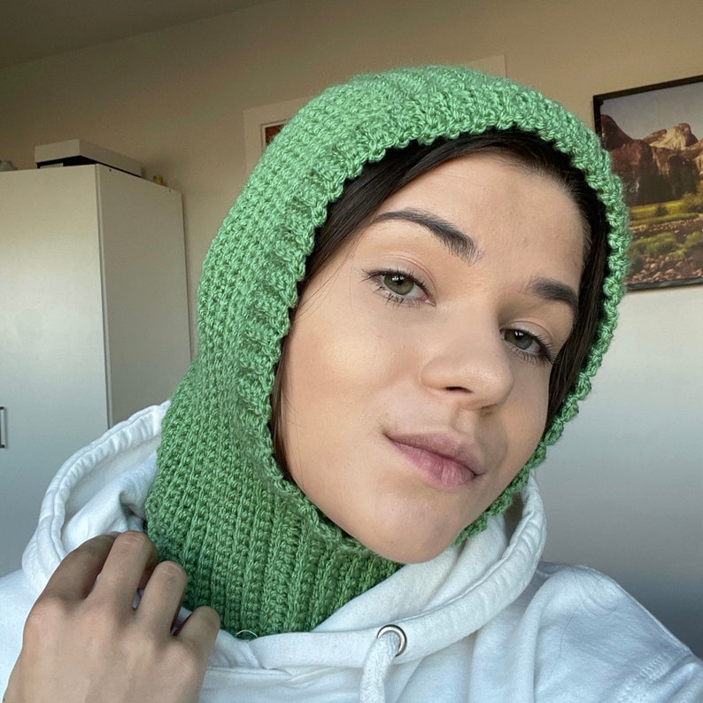May include: A green crocheted hooded neck warmer. The neck warmer is made of a soft, textured yarn and has a simple, classic design.