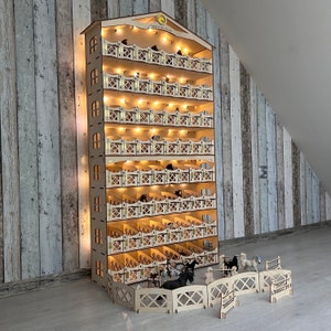 May include: A wooden horse stable with multiple levels and lights. The stable is made of light wood and has a white fence around it. There are several small toy horses inside the stable.