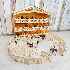 Pode incluir: Um brinquedo de estábulo de cavalos de madeira com vários estábulos, cada um com um cavalo de brinquedo. O conjunto inclui uma cerca de madeira, saltos e figuras de brinquedo. O estábulo tem um relógio e uma luz.