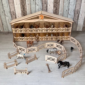 May include: Wooden toy stable with a sign that reads "Dolly's Stables" and multiple horse stalls. The stable is surrounded by a wooden fence and includes several toy horses and fences.