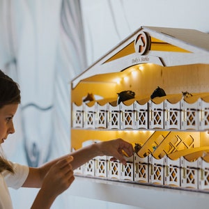 May include: A wooden toy stable with a white roof and a sign that reads "Dolly's Stables". The stable has two levels of stalls with small horses inside. A young girl is reaching into one of the stalls.