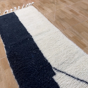 Pu&ograve; includere: Un tappeto bianco e nero con un design geometrico. Il tappeto &egrave; fatto di lana e ha una texture morbida e soffice.