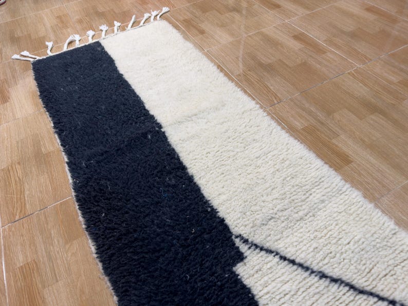 Pu&ograve; includere: Un tappeto bianco e nero con un design geometrico. Il tappeto &egrave; fatto di lana e ha una texture morbida e soffice.