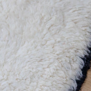 May include: Close-up of a white, fluffy rug with a black border. The rug has a thick, textured pile, creating a soft and inviting appearance. The contrasting black border adds a modern touch to the design.