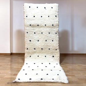 Puede incluir: Una alfombra blanca con un patrón de lunares negros. La alfombra está hecha de un material suave y esponjoso y tiene un borde con flecos.