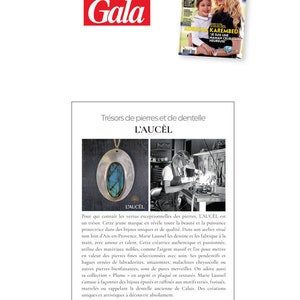 May include: A silver pendant necklace with a blue-green stone set in a silver oval. The pendant is on a silver chain. The image is from a magazine article about the jewellery brand L'Au&ccedil;el.