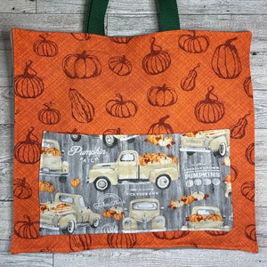 Puede incluir: Bolsa de tela naranja con un diseño de campo de calabazas. La bolsa tiene un asa de lona verde y un bolsillo con un diseño de camión vintage. El bolsillo tiene el texto "Pumpkin Patch" y "Farm Fresh Pick Your Own" y "Locally Grown Fresh and Delicious Pumpkins".