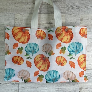 Może przedstawiać: Prostokątna torba z białymi uchwytami i powtarzającym się wzorem pomarańczowych, turkusowych i beżowych dyni, wraz z pomarańczowymi i zielonymi liśćmi, na białym tle. Torba jest wykonana z tkaniny.