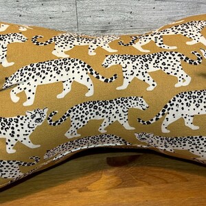 May include: Mustard-colored neck pillow with a repeating pattern of white and black leopard print. The pillow is shaped like a figure eight, designed for neck support and comfort.