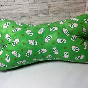 May include: Green dog bed shaped like a bone with a pattern of white coffee cups with whipped cream and sprinkles on a green background.
