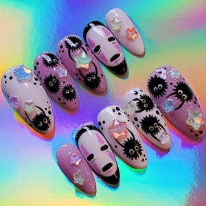 Può includere: Set di dieci unghie finte con uno schema di colori rosa e bianco. Le unghie presentano un'illustrazione in bianco e nero di un personaggio senza volto del film La città incantata e un'illustrazione in bianco e nero di uno spirito di fuliggine. Le unghie sono decorate con glitter iridescente e strass.