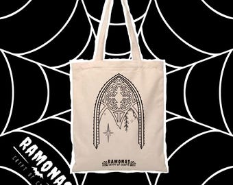 May include: A white tote bag with black handles and a black line drawing of an arched window with a star and vines. The text "Ramonas Crypt of Crafts" is printed on the bag.
