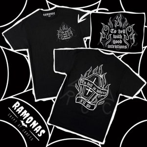 Può includere: Due t-shirt nere con disegni grafici bianchi. La maglietta anteriore presenta un disegno di fiamme con il testo "To hell with good intentions". La maglietta posteriore presenta un disegno di una bara con fiamme e il testo "To hell is where I'll go".