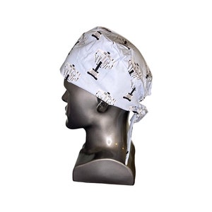 Pode incluir: Um gorro cir&uacute;rgico azul claro com um design estampado em branco e preto. O gorro tem um la&ccedil;o na parte de tr&aacute;s.