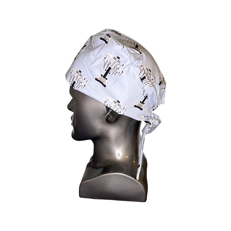 Pode incluir: Um gorro cir&uacute;rgico azul claro com um design estampado em branco e preto. O gorro tem um la&ccedil;o na parte de tr&aacute;s.