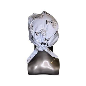 Pode incluir: Um gorro cir&uacute;rgico azul claro com um padr&atilde;o preto e branco de formas abstratas. O gorro &eacute; amarrado na parte de tr&aacute;s da cabe&ccedil;a.