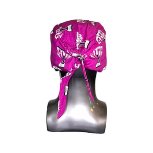 Pode incluir: Um gorro cir&uacute;rgico rosa com uma estampa branca de halteres. O gorro tem um la&ccedil;o na parte de tr&aacute;s.