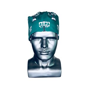 Pode incluir: Um gorro de cirurgia verde com uma estampa gr&aacute;fica branca de um s&iacute;mbolo m&eacute;dico. O gorro est&aacute; em uma cabe&ccedil;a de manequim prateada.