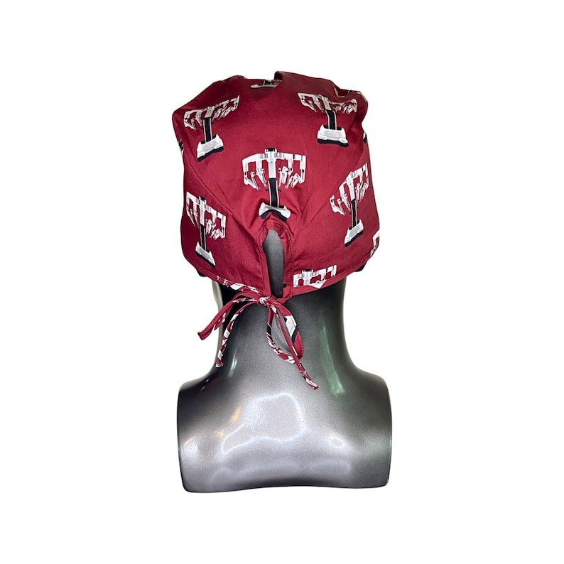 Pode incluir: Um gorro cir&uacute;rgico vermelho com uma estampa branca de um s&iacute;mbolo m&eacute;dico. O gorro tem um la&ccedil;o na parte de tr&aacute;s.