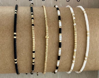 May include: Six beaded bracelets in black, white, and gold. The bracelets are numbered 1 through 6.