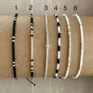 Puede incluir: Seis pulseras de cuentas en negro, plata y blanco. Las pulseras están numeradas del 1 al 6.