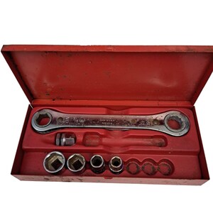 May include: A red metal tool box containing a silver ratcheting wrench marked 5/8, a square drive adapter, and four various sized metal sockets. The interior of the box features a molded red plastic insert designed to hold each tool securely in place.